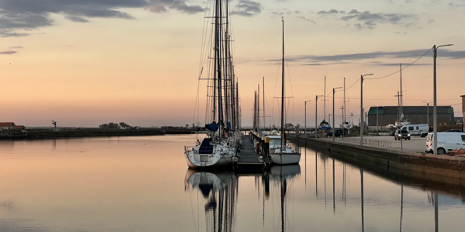 Veleiros atracados em Aveiro ao entardecer, refletidos na água.